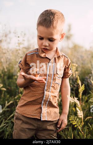 Un bambino piccolo tiene una lumaca nelle sue mani e la esamina attentamente Foto Stock