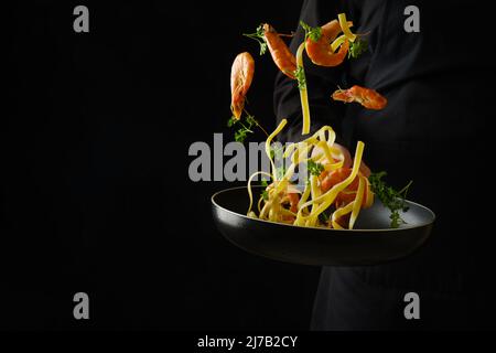 Il processo di cottura della pasta con frutti di mare e verdure da parte di uno chef professionista su sfondo nero. Cibo congelato a bordo. Sfondo alimentare. Sano Foto Stock