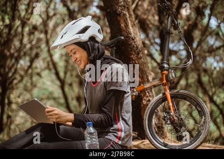 donna velata sorridente indossando gli auricolari mentre si è seduti a riposare Foto Stock