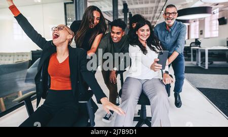 Cattura i migliori momenti di lavoro. Donna d'affari felice che prende un selfie con i suoi colleghi durante il periodo di gioco. Gruppo di uomini d'affari che si divertono e celebrano Foto Stock