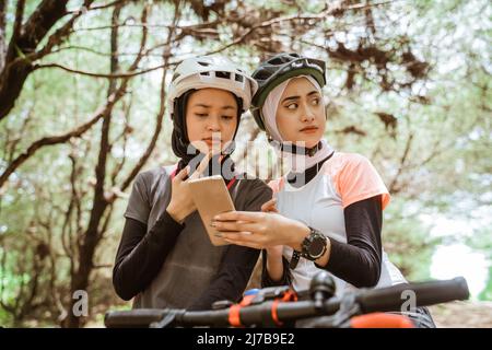 Due donne musulmane che ciclano confusi mentre usano un telefono cellulare Foto Stock