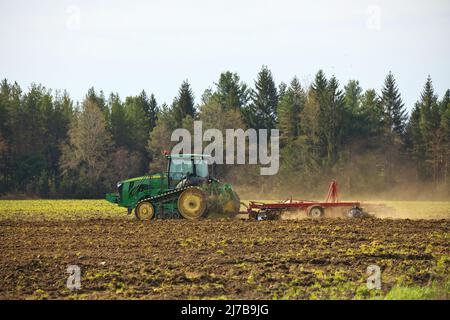 Trattore cingolato per arare il campo con erpice in primavera in azienda agricola con nubi di polvere Foto Stock