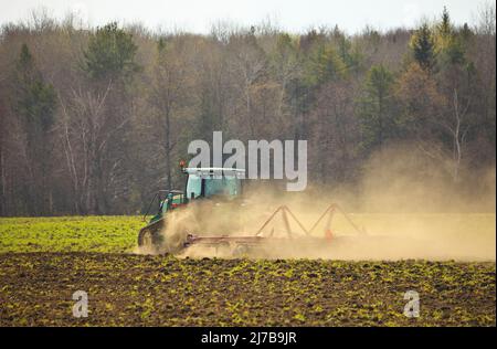 Trattore cingolato per arare il campo con erpice in primavera in azienda agricola con nubi di polvere Foto Stock