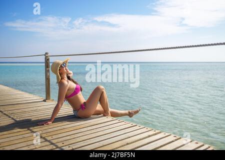 felice giovane donna in cappello di paglia seduto su pontone in legno Foto Stock