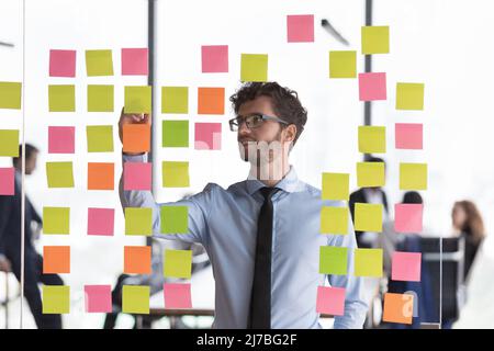 Sorridente uomo d'affari ha messo a fuoco giovane che scrive le note sul bordo di vetro Foto Stock