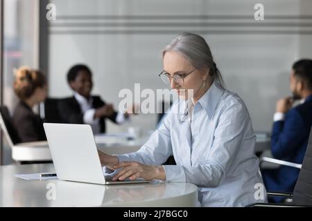 Donna professionale di mezza età focalizzata in occhiali utilizzando il laptop Foto Stock