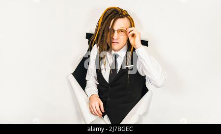 Giovane uomo in occhiali che guarda in lontananza, in piedi nel buco di fondo bianco. Bel maschio in camicia bianca, gilet nero e cravatta cercando di vedere il thru Foto Stock