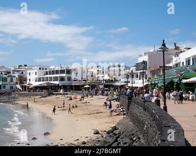 Playa Blanca, Spagna; marzo 26th 2022: Playa Blanca, città turistica di Lanzarote. I turisti prendono il sole sulla spiaggia e camminano lungo il lungomare Foto Stock