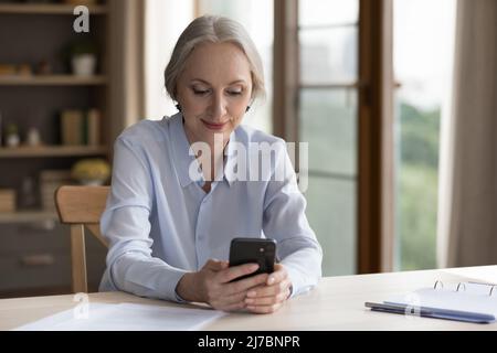 Felice donna d'affari matura che usa l'app online sul telefono cellulare Foto Stock