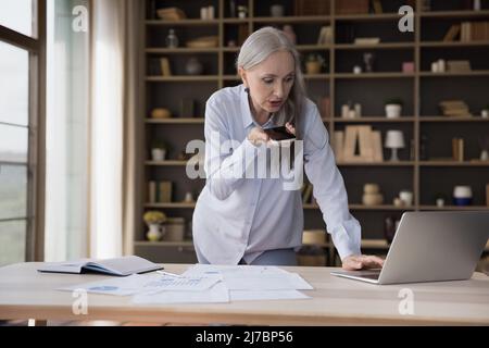 Donna professionale seria occupata matura di affari in piedi al tavolo Foto Stock