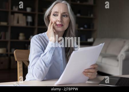 Pensierosa donna d'affari di mezza età preoccupata che tiene i documenti cartacei Foto Stock