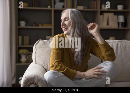 Allegro maturo 50s donna seduta sul divano a casa Foto Stock