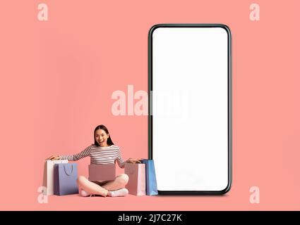 Donna in posa con schermo bianco vuoto per smartphone e borse per gli acquisti Foto Stock