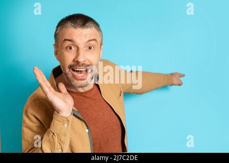 Uomo di età media puntando dito a lato di pubblicità offerta, sfondo blu Foto Stock