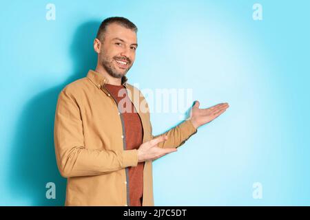 Sorridente uomo di mezza età gesturing puntando da parte su sfondo blu Foto Stock