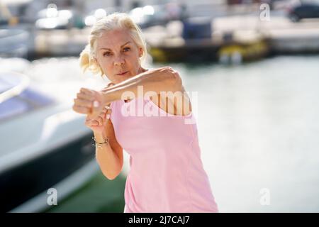 Donna anziana che fa la boxe ombra all'aperto. Donna anziana che fa sport in un porto costiero Foto Stock