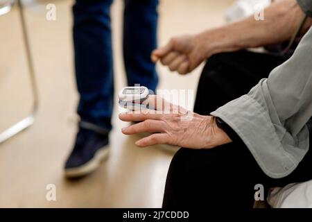 Dettagli con la mano di un paziente anziano che indossa un pulsossimetro sul dito presso il gabinetto del medico. Foto Stock