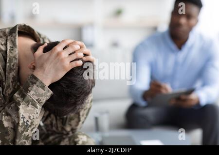 Depresso soldato visita psicoterapeuta in clinica, coprendo la testa con le mani Foto Stock