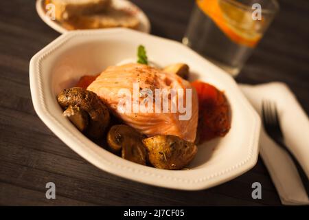 filetto di salmone al vapore su un cuscino di funghi fritti e pomodori in un recipiente bianco Foto Stock