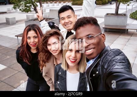 Da sopra l'uomo afroamericano sorridendo e prendendo un selfie con amici multirazziali in una giornata di fine settimana sulla strada. Foto Stock