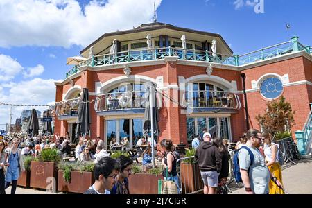 Brighton UK 8th May 2022 - i bar e ristoranti sul lungomare, tra cui la Shelter Hall, sono occupati mentre i visitatori godono di una calda giornata di sole sulla spiaggia di Brighton, come si prevede che le temperature raggiungano oltre 20 gradi in alcune parti del Regno Unito: Credit Simon Dack / Alamy Live News Foto Stock