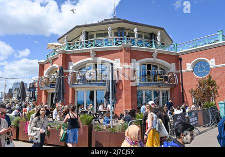 Brighton UK 8th May 2022 - i bar e ristoranti sul lungomare, tra cui la Shelter Hall, sono occupati mentre i visitatori godono di una calda giornata di sole sulla spiaggia di Brighton, come si prevede che le temperature raggiungano oltre 20 gradi in alcune parti del Regno Unito: Credit Simon Dack / Alamy Live News Foto Stock