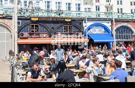 Brighton UK 8th May 2022 - i bar e i ristoranti sul lungomare sono occupati come i visitatori godono di una calda giornata di sole sulla spiaggia di Brighton come si prevede che le temperature raggiungano oltre 20 gradi in alcune parti del Regno Unito: Credit Simon Dack / Alamy Live News Foto Stock