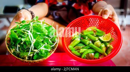 Peperoncini verdi tagliati a fette in un recipiente rosso accanto a lime tagliate. Foto Stock