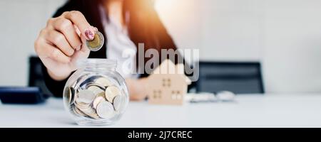 primo piano mano di donna salvare e mettere monete in bottiglia in vetro, risparmiare finanze e bilancio concetto di banca Foto Stock