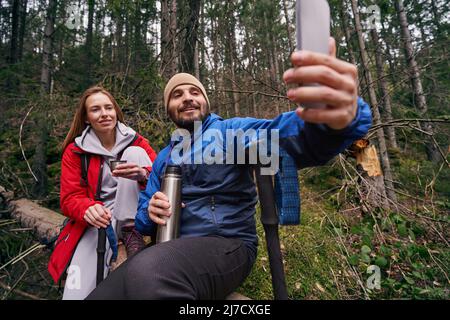Due escursionisti su albero facendo selfie nei boschi Foto Stock