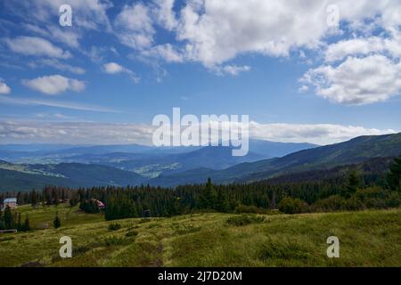 Piccolo villaggio di montagna, con pochi cottage in fitta foresta di conifere in autunno. Vista panoramica del villaggio remoto in montagna, con magnifico paesaggio sullo sfondo. Concetto di altopiano. Foto Stock