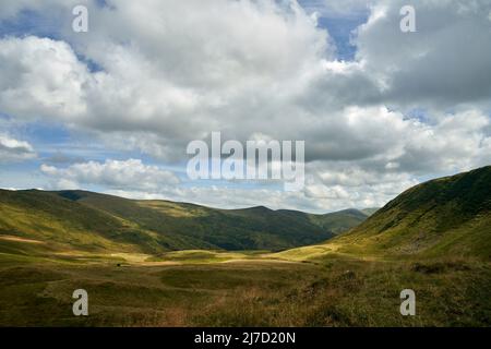 Enormi nuvole ombre galleggianti su prati verdi di zona collinare all'aperto. Vista panoramica delle aree montagnose che si estendono su ampie nuvole di cumuli che attraversano il cielo blu in estate. Concetto di paesaggio. Foto Stock