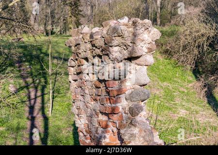 Parte di un vecchio muro di mattoni stagionato in un'area rurale. Un relitto edilizio del Medioevo in Europa. Le pietre sono intemperie e in cattive condizioni. Foto Stock