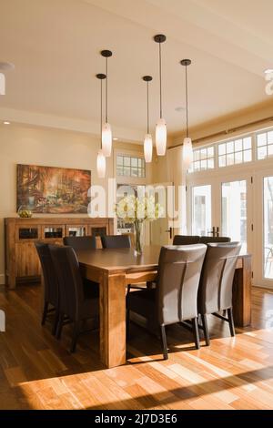 Tavolo da pranzo in legno e sedie in pelle marrone con schienale alto nella sala da pranzo all'interno di una lussuosa casa. Foto Stock