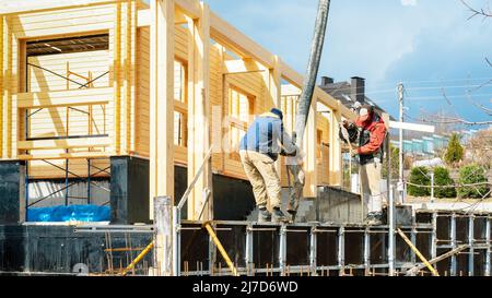 I lavoratori cementano la parete di contenimento e la fondazione per la terrazza utilizzando casseforme e ponteggi. Cantiere di costruzione di una casa in legno di b incollato Foto Stock