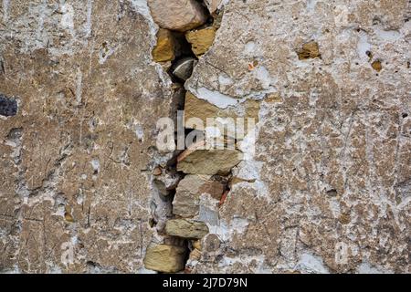 Una grande crepa sul muro di una vecchia casa, intonaco sbriciolato e mattoni rotti e spaccati. Immagine di sfondo. Foto Stock