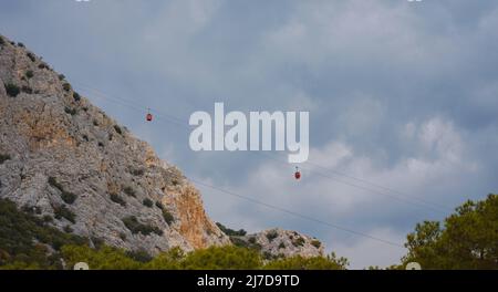 Cabine rosse di funicolare ad Antalya, Turchia sullo sfondo di nuvole di pioggia. Gita in funivia ai punti panoramici delle montagne. Durante il viaggio in funivia i turisti godono di splendide vedute della città e della natura Foto Stock