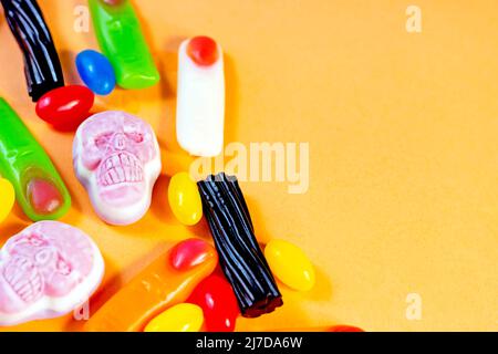 Diversi dolci di gelatina di Halloween (teschi, dita zombie e fagioli) come una cornice su sfondo arancione con spazio copia. Foto Stock