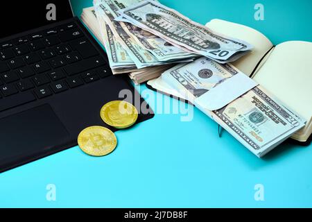 Computer portatile nero con alcuni bitcoins su di esso, un notebook con una bacchetta di dollari su un tavolo blu con spazio copia. Foto in formato orizzontale. Foto Stock