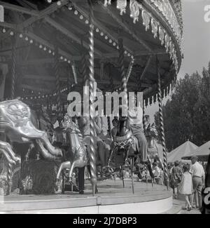 1960s, storico, persone che cavalcano su un carosello o allegro-go-round ad un funfair, Inghilterra, Regno Unito. Foto Stock