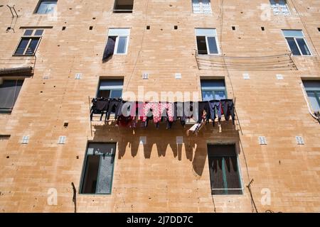 Stringa di vestiti appesi sulla parete soleggiata di un palazzo Foto Stock