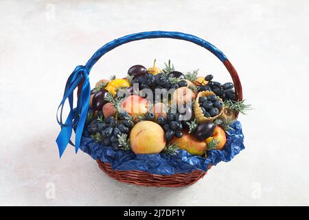 Cestino pieno di uva e altri frutti su sfondo grigio Foto Stock