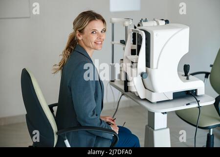 Paziente donna sorridente attende un test di visione presso il negozio di ottico o clinica oftalmologica Foto Stock