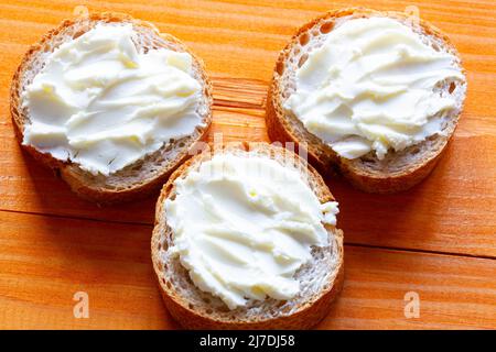 Panini con formaggio cremoso sul tavolo. Fette di pane con formaggio morbido spalmato. Pasta spalmata su una baguette francese fresca. Dessert fatto in casa Foto Stock