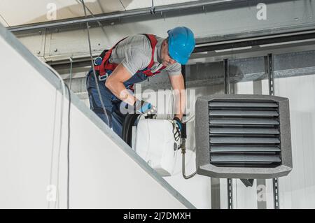 Impiegato tecnico HVAC caucasico nel suo 40s Installazione di riscaldatori aria e acqua all'interno di un magazzino di nuova costruzione. Foto Stock