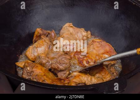 Processo di cottura della carne di agnello per pilaf, pilau in cauldron enorme Foto Stock