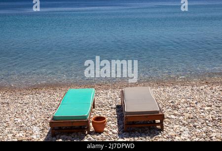 Due lettini vuoti su una piccola spiaggia di pietra sul mare. Concetto di vacanza. Foto Stock