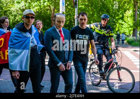 Un poliziotto olandese sulla sua moto guarda un uomo vestito mentre Putin passa accanto durante la manifestazione. Il 8 maggio, le diaspore russe in diversi paesi hanno condotto azioni anti-belliche a sostegno dell'Ucraina. All’Aia, di fronte all’Ambasciata russa, si è svolta una marcia per la costruzione della Corte internazionale di giustizia (ICJ), per un processo simbolico contro Putin. Queste azioni sono vicine al 9 maggio (noto come Giornata della Vittoria all'interno della Russia) per fare una dichiarazione contro il regime di Putin, che si è trasformato questa giornata in una celebrazione del militarismo, normalizzando la guerra e usandola per servire la sua Foto Stock