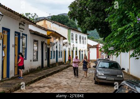 Vista sulla strada Direita con una fila di case coloniali affiancate e pedoni che camminano nel centro storico di Tiradentes sotto il cielo nuvoloso. Foto Stock