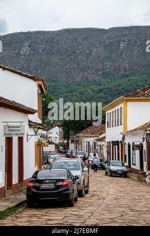 Vista della strada Direita con auto parcheggiate presso edifici coloniali nel centro storico di Tiradentes sotto il cielo nuvoloso. Foto Stock